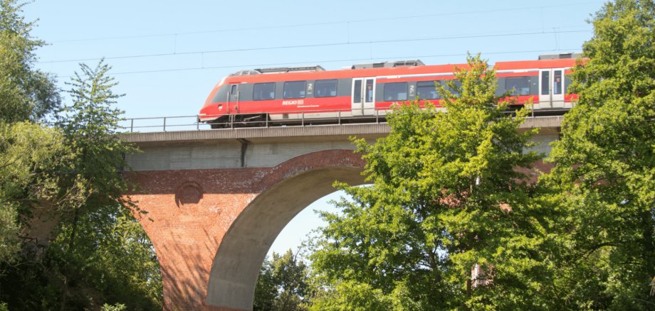Eine rote Bahn fahrend über einen Viadukt umgeben von Bäumen