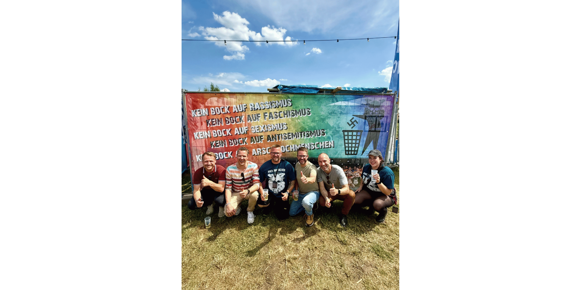 Fünf Männer und eine Frau knieend und lächelnd auf einem Acker vor einem bunten Banner.