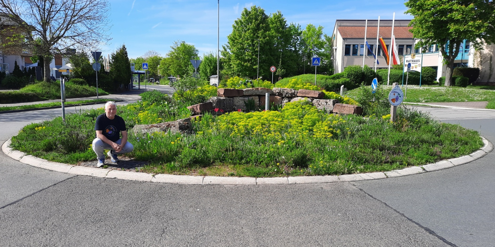 Mann kniend vor blühendem Verkehrskreisel