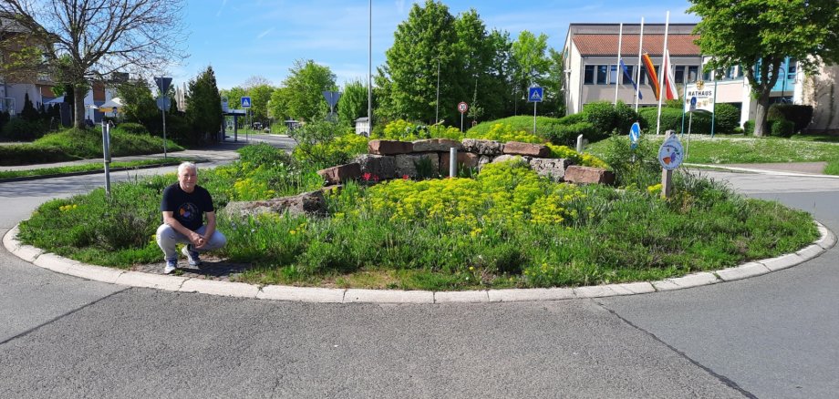 Mann kniend vor blühendem Verkehrskreisel