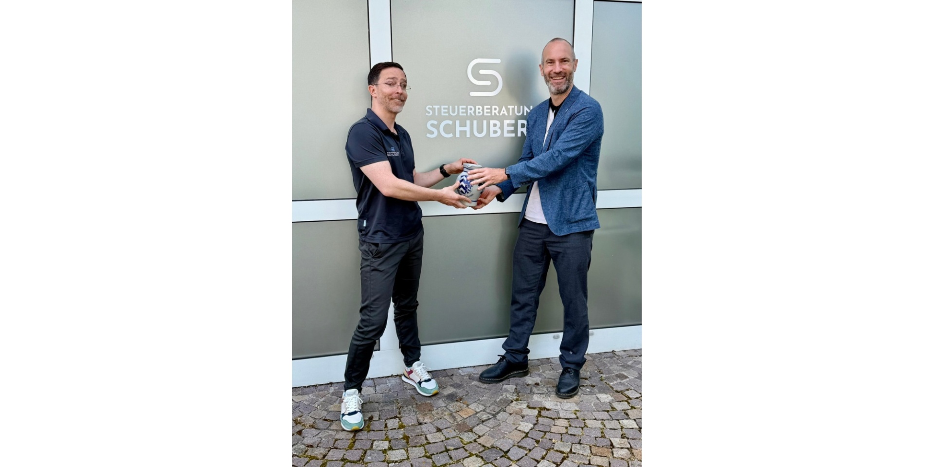 Zwei Männer stehend. Der eine überreicht dem anderen einen hessischen Krug (Bembel).