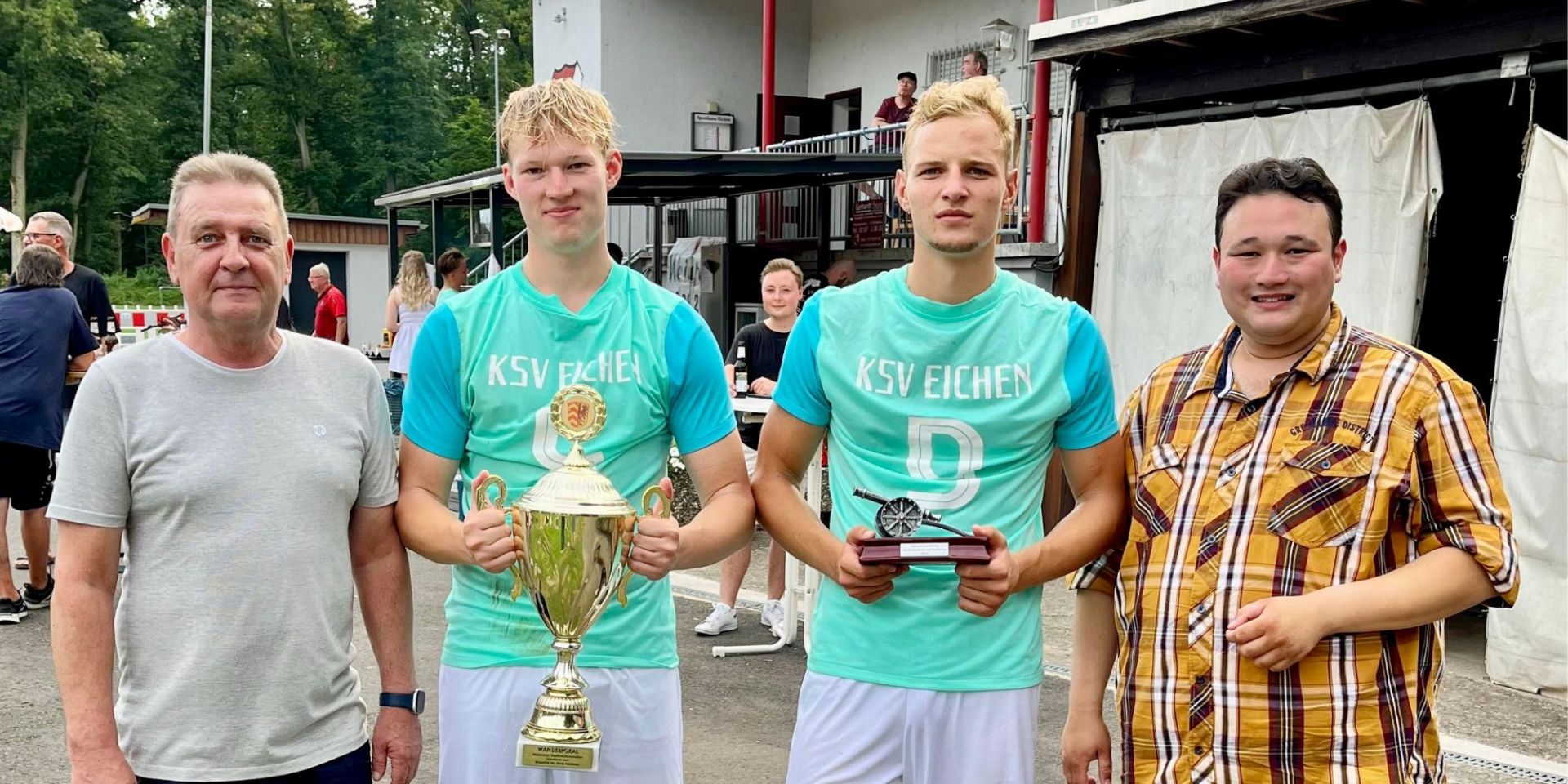 Vier Männer, zwei davon halten einen Pokal