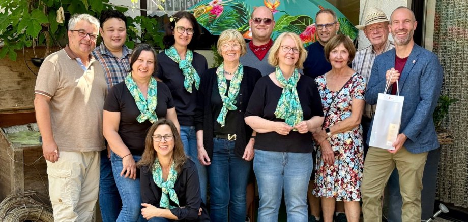 Mehrere Personen stehend vor einer Hausfassade. Davon tragen 4 Frauen schwarze Oberteile mit grün-blauen Halstüchern