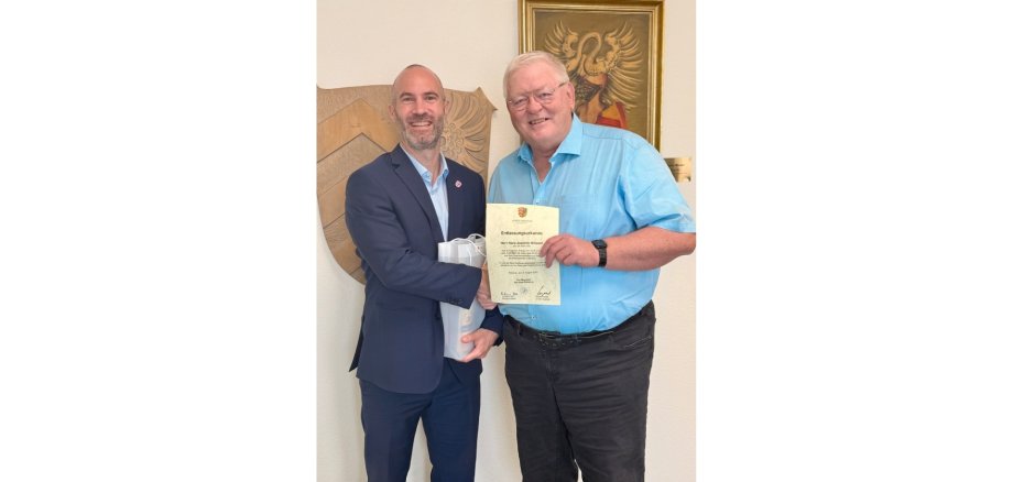 Zwei Männer stehend nebeneinander. Ein Mann hält eine Urkunde in der Hand