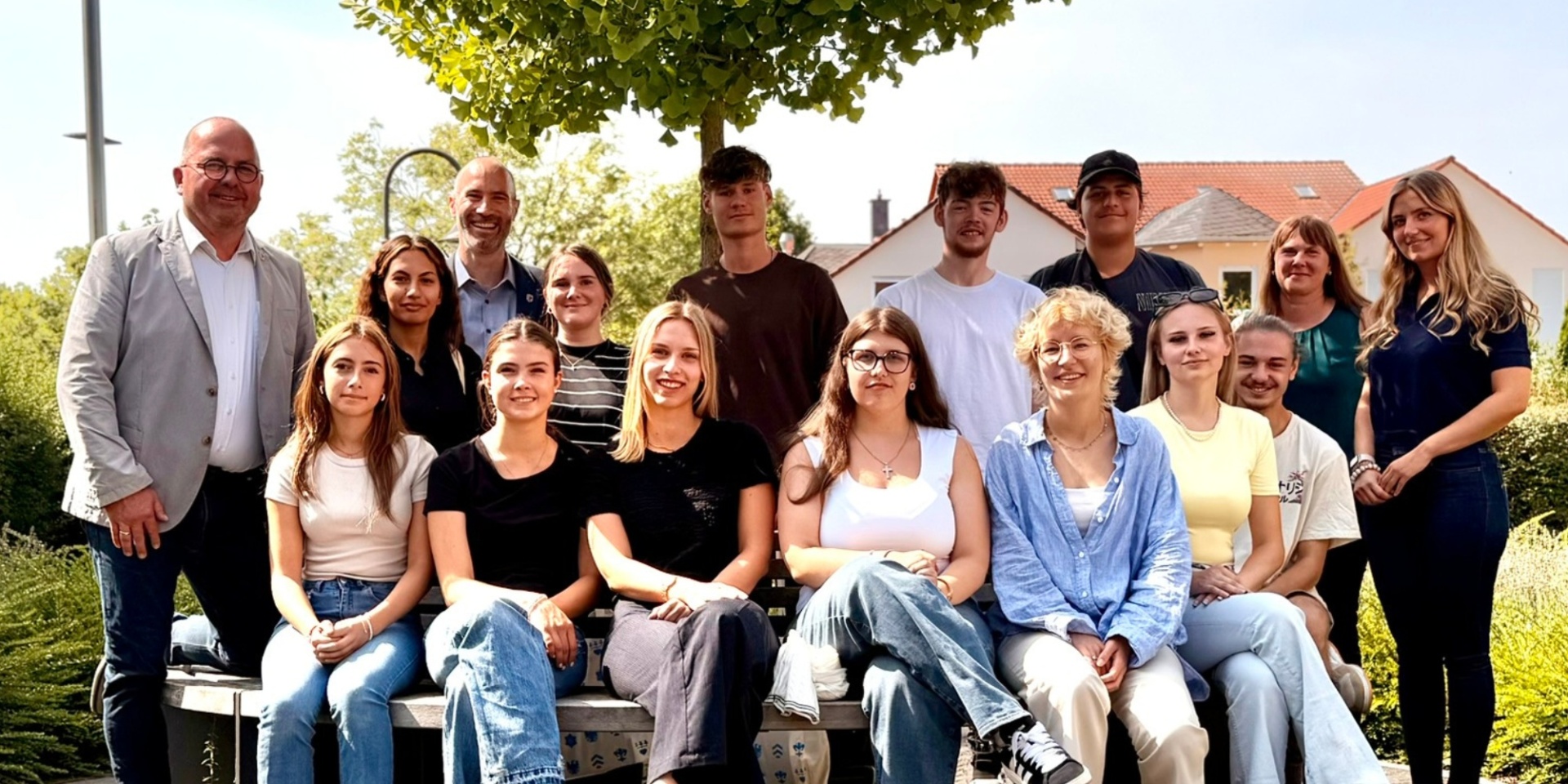 Mehrere Jugendliche sitzend und stehend draußen vor dem Rathaus. Im Hintergrund ein Baum