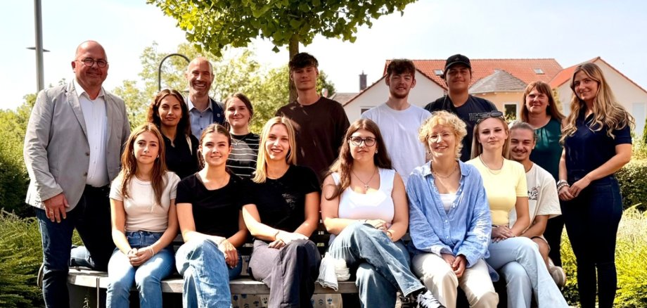 Mehrere Jugendliche sitzend und stehend draußen vor dem Rathaus. Im Hintergrund ein Baum