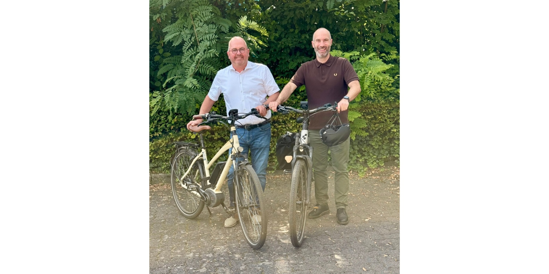 Zwei Männer mit Fahrrädern vor einer Hecke