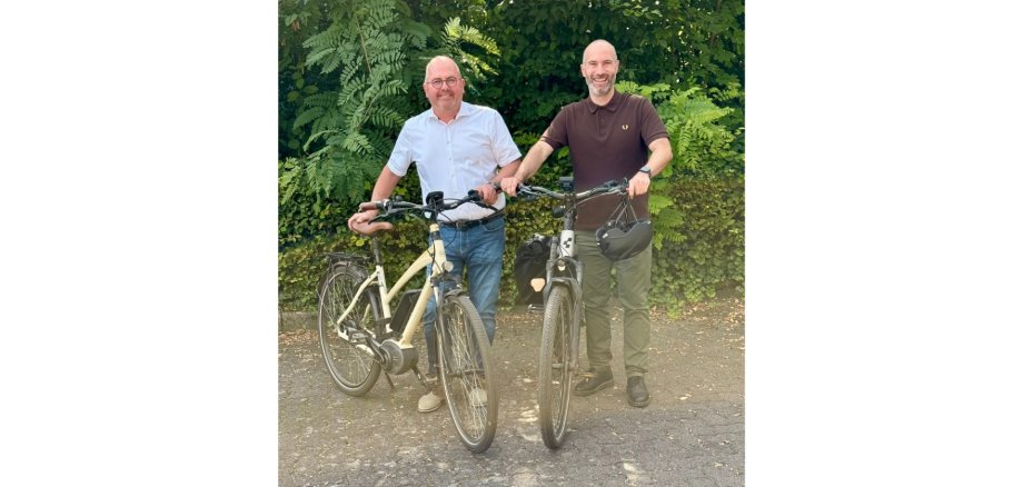 Zwei Männer mit Fahrrädern vor einer Hecke