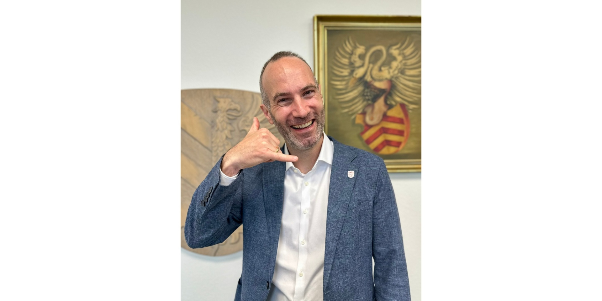 Lächelnder Mann im Anzug und Hemd macht eine Handgeste als Telefonhörer zum Ohr