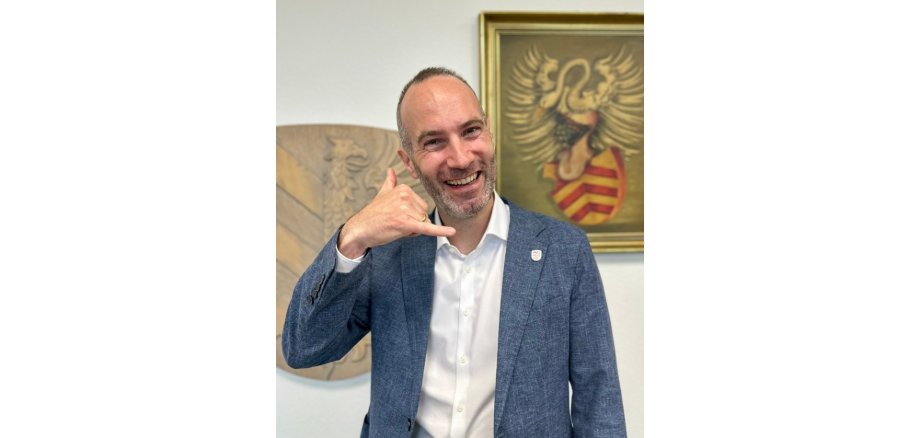 Lächelnder Mann im Anzug und Hemd macht eine Handgeste als Telefonhörer zum Ohr