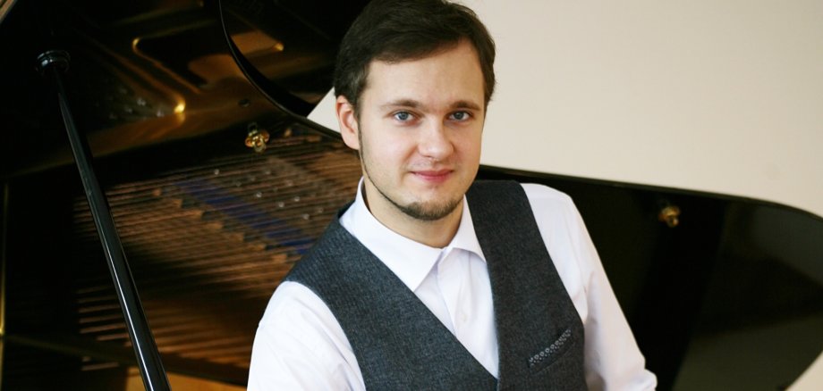 Mann in schwarz-weiß gekleidet sitzt vor einem Flügel