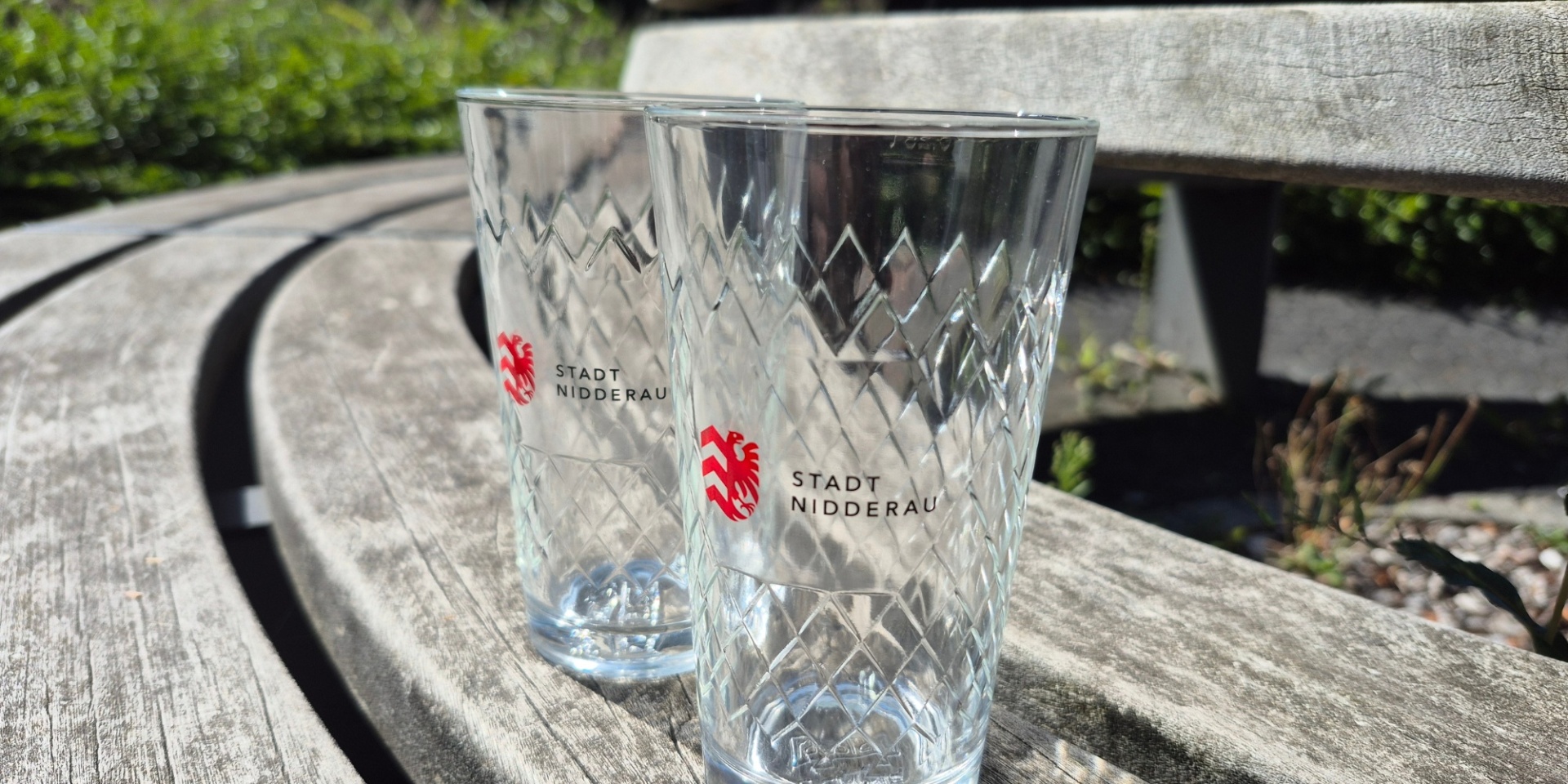 Zwei Apfelweingläser mit Nidderau-Logo auf einer Holzbank stehend