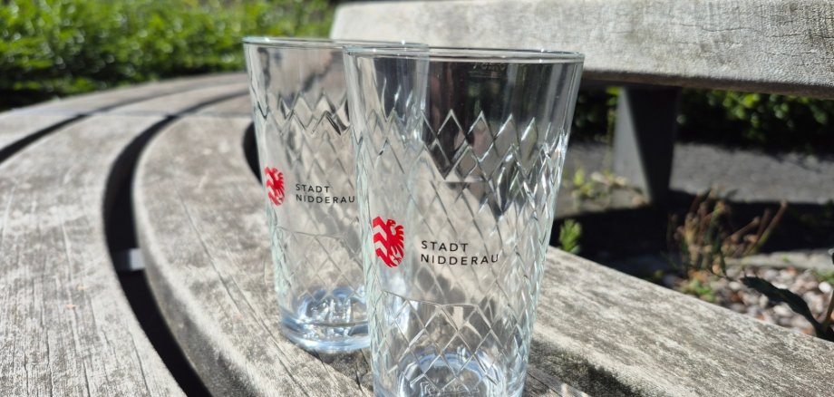 Zwei Apfelweingläser mit Nidderau-Logo auf einer Holzbank stehend