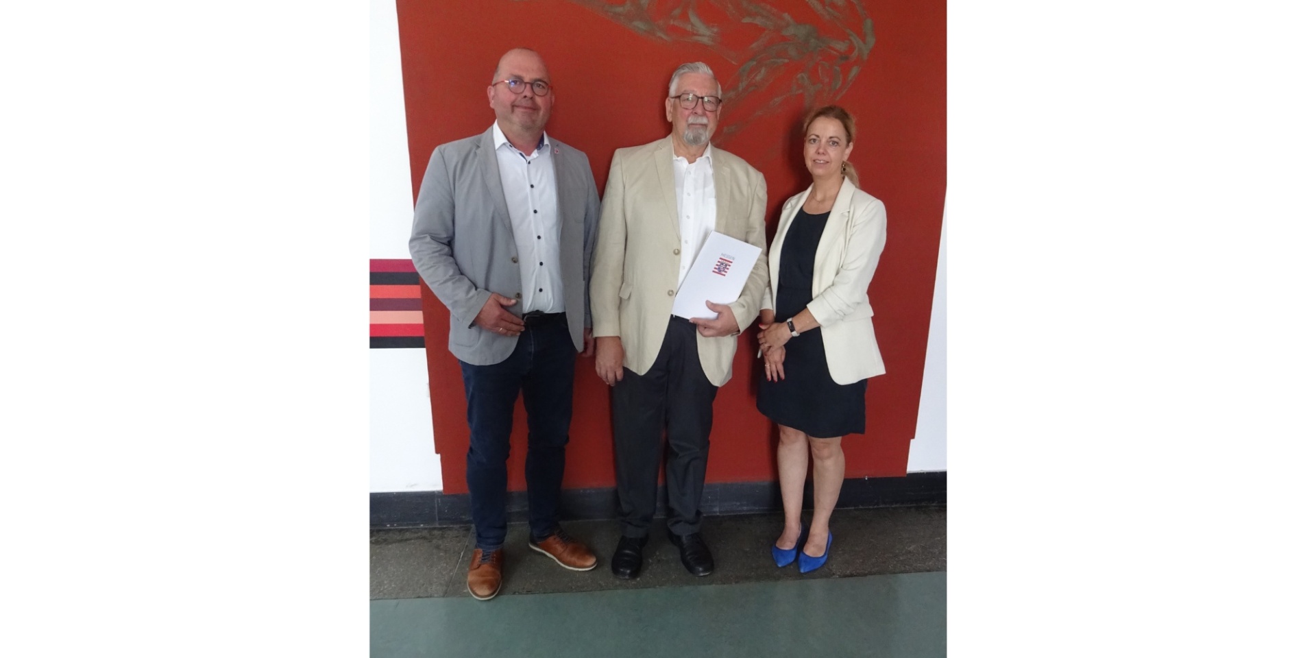 Zwei Männer und eine Frau stehend vor einem roten Hintergrund