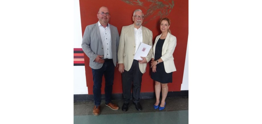 Zwei Männer und eine Frau stehend vor einem roten Hintergrund