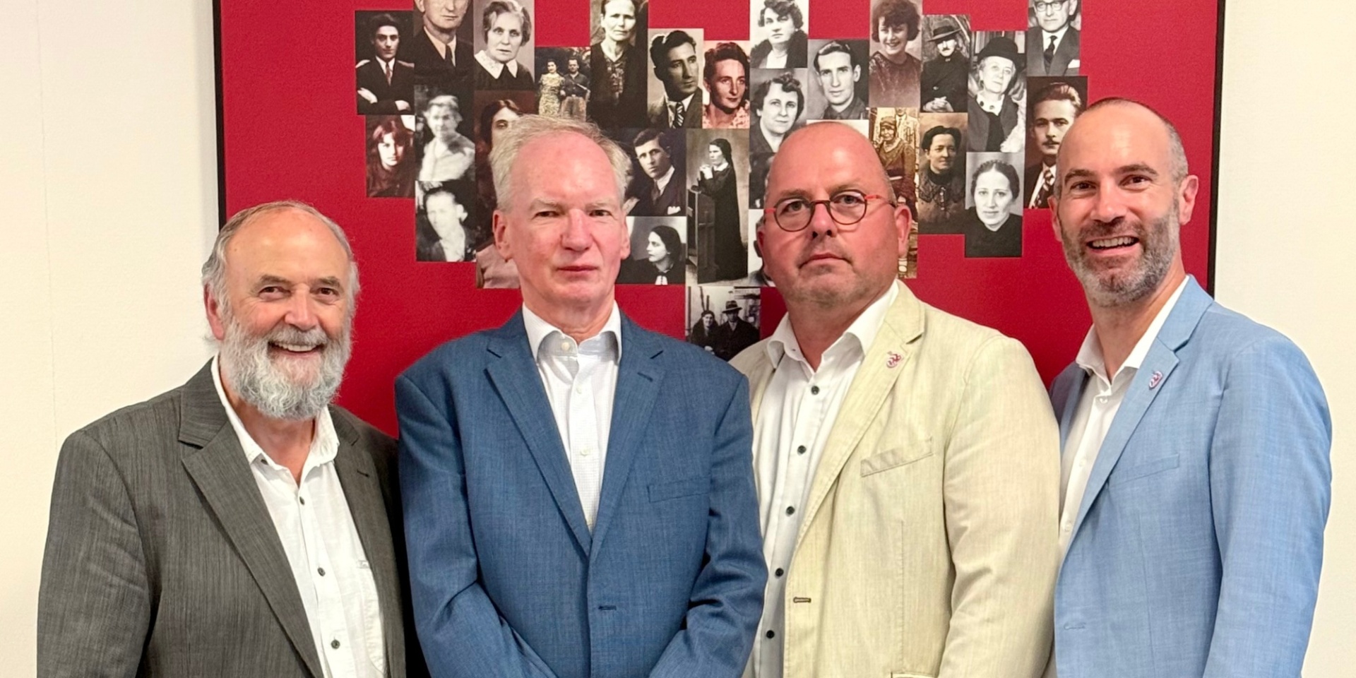 Vier Männer stehend vor einem roten Hintergrund