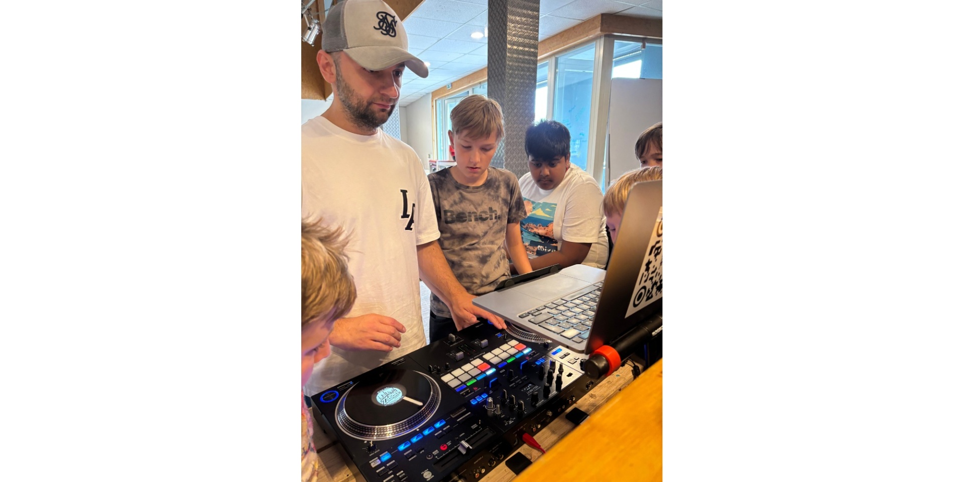 Mann mit Baseballcap vor einem Mischpult und nebendran interessierte Jungen