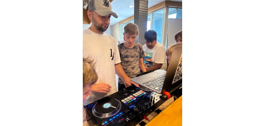 Mann mit Baseballcap vor einem Mischpult und nebendran interessierte Jungen