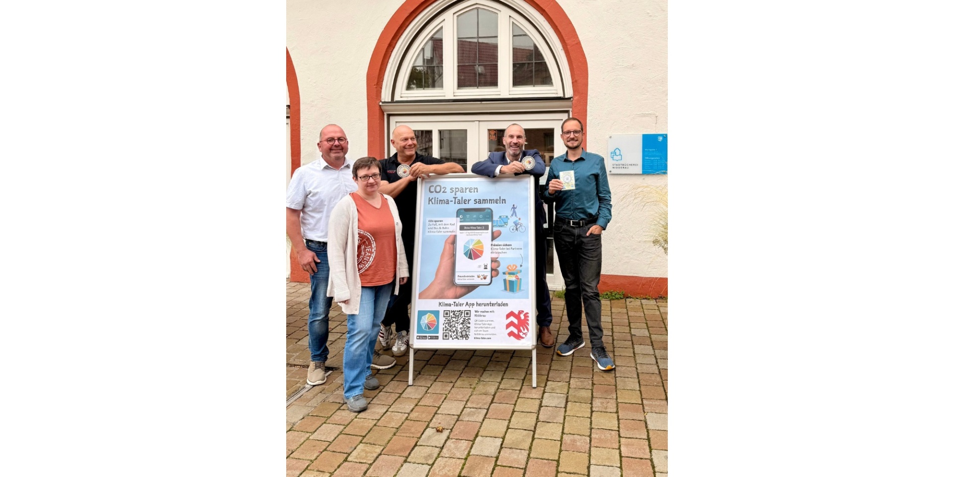 Eine Frau und vier Männer stehend um eine Reklametafel