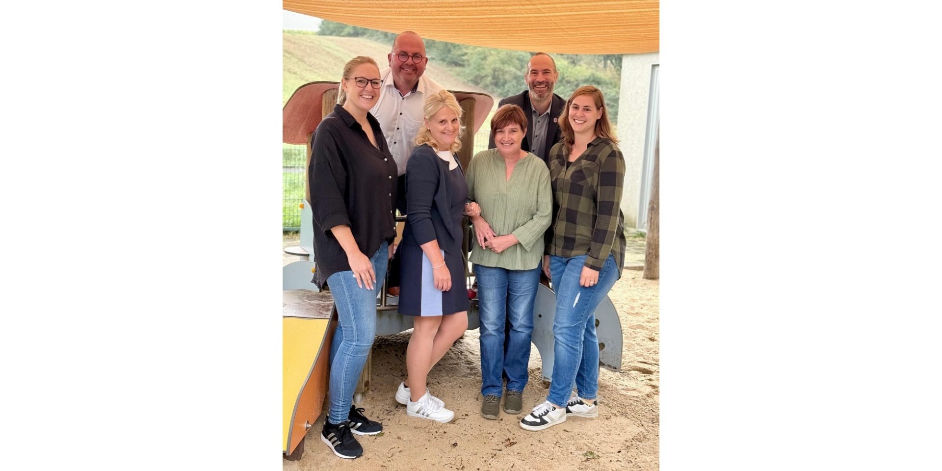 Vier Frauen und zwei Männer stehend im Sand vor einem Kinderspielgerüst.