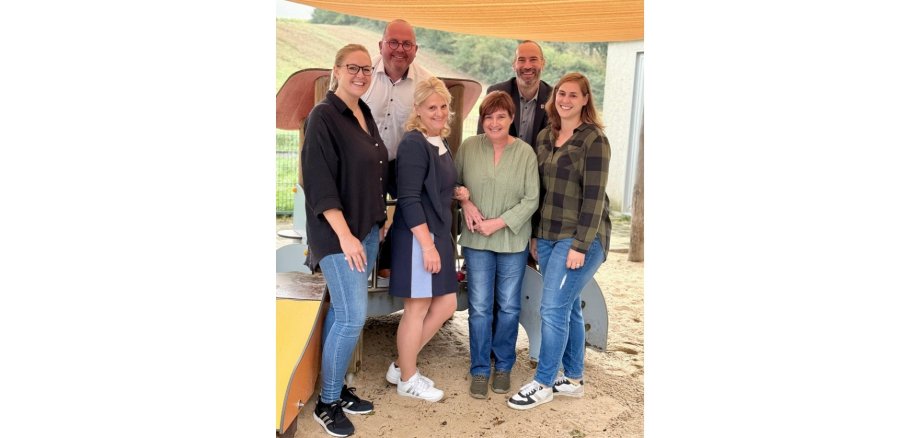 Vier Frauen und zwei Männer stehend im Sand vor einem Kinderspielgerüst.