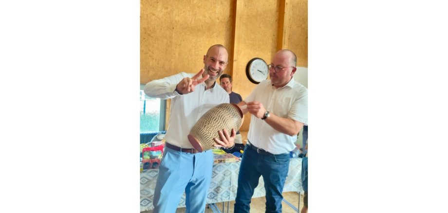 Zwei Männer stehend. Der eine Mann hält eine große Vase in der Hand