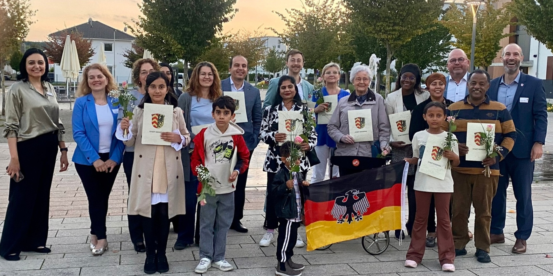 Mehrere Personen stehend auf einem Platz. Einige halten Urkunden in der Hand und lächeln