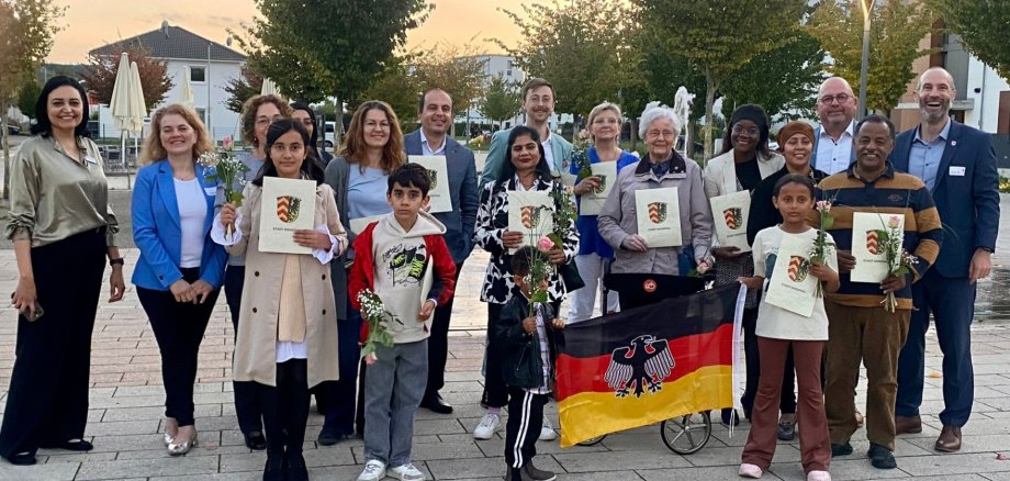 Mehrere Personen stehend auf einem Platz. Einige halten Urkunden in der Hand und lächeln
