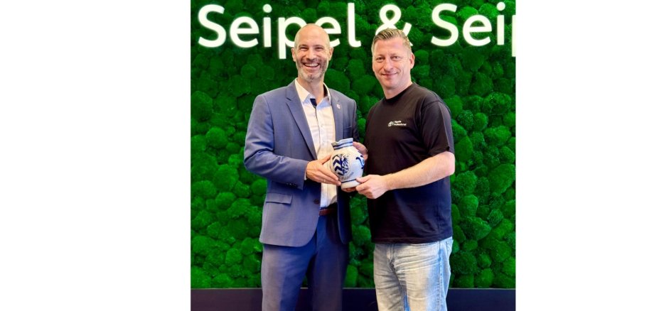 Zwei Männer stehend vor einem grünen Hintergrund.