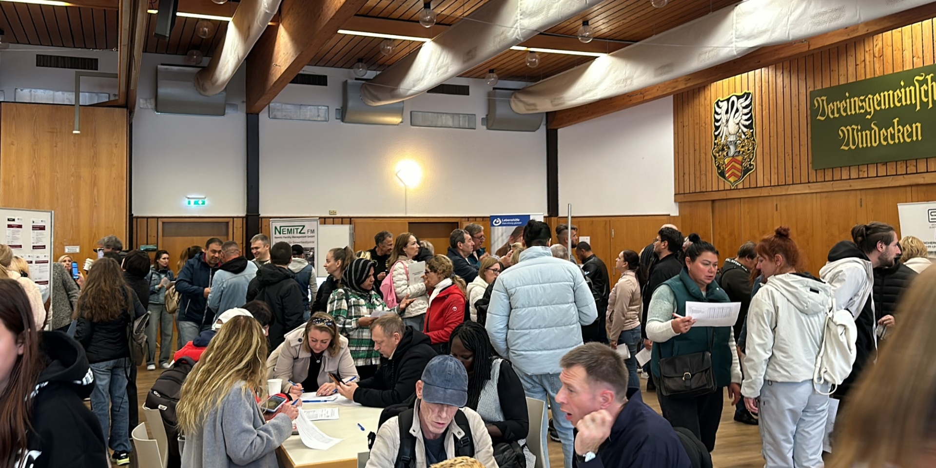 Viele Menschen stehend oder sitzend in einer Bürgerhalle