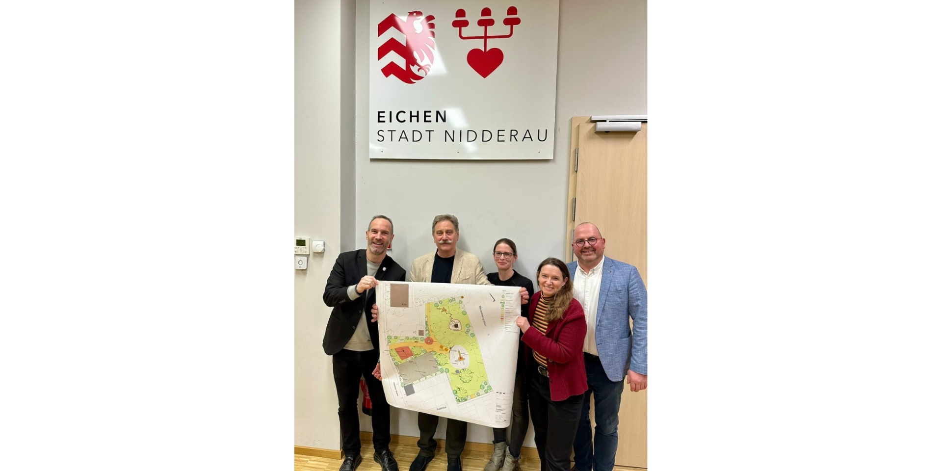 Zwei Frauen und drei Männer stehend mit einem Plakat, welches einen Bebauungsplan zeigt