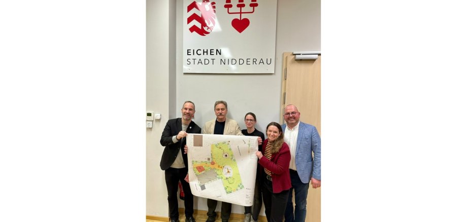 Zwei Frauen und drei Männer stehend mit einem Plakat, welches einen Bebauungsplan zeigt