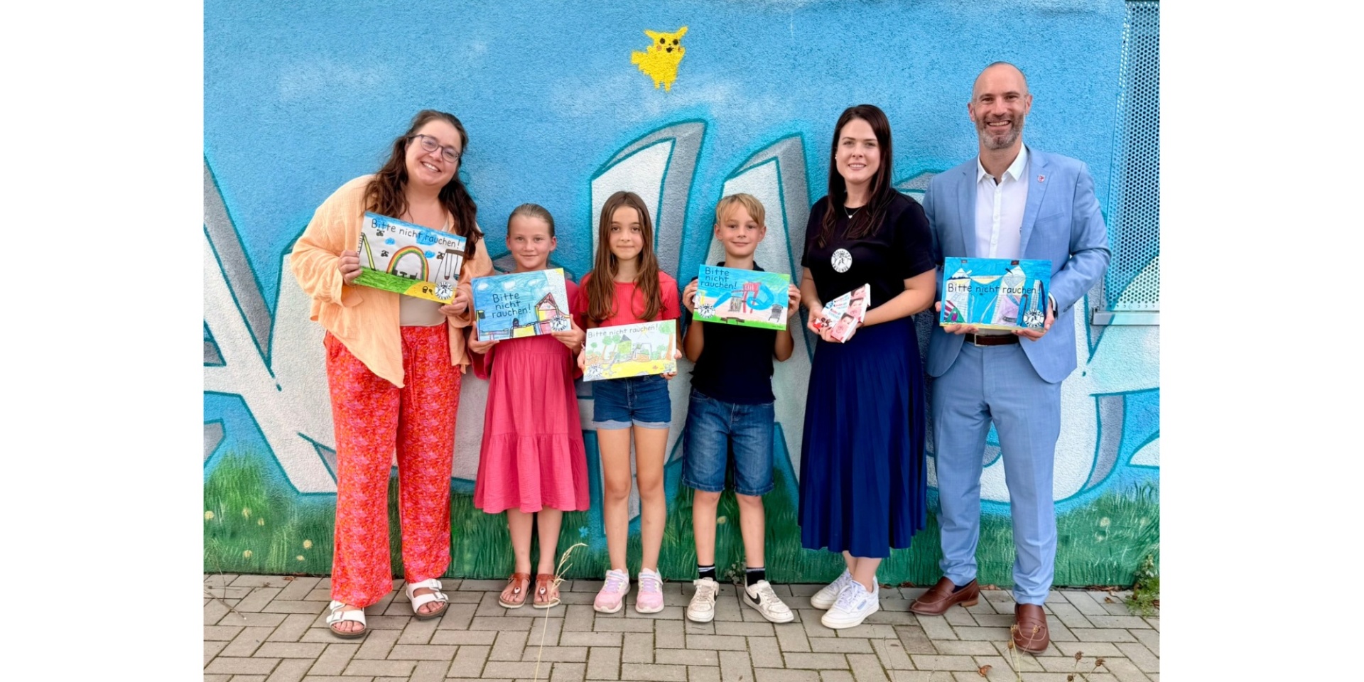 Zwei Frauen, drei Kinder und ein Mann stehend vor einer blauen Außenwand. 