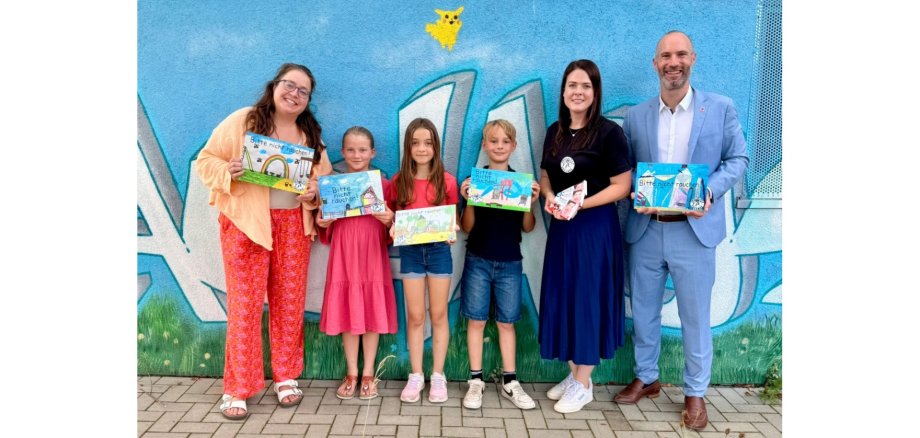 Zwei Frauen, drei Kinder und ein Mann stehend vor einer blauen Außenwand. 