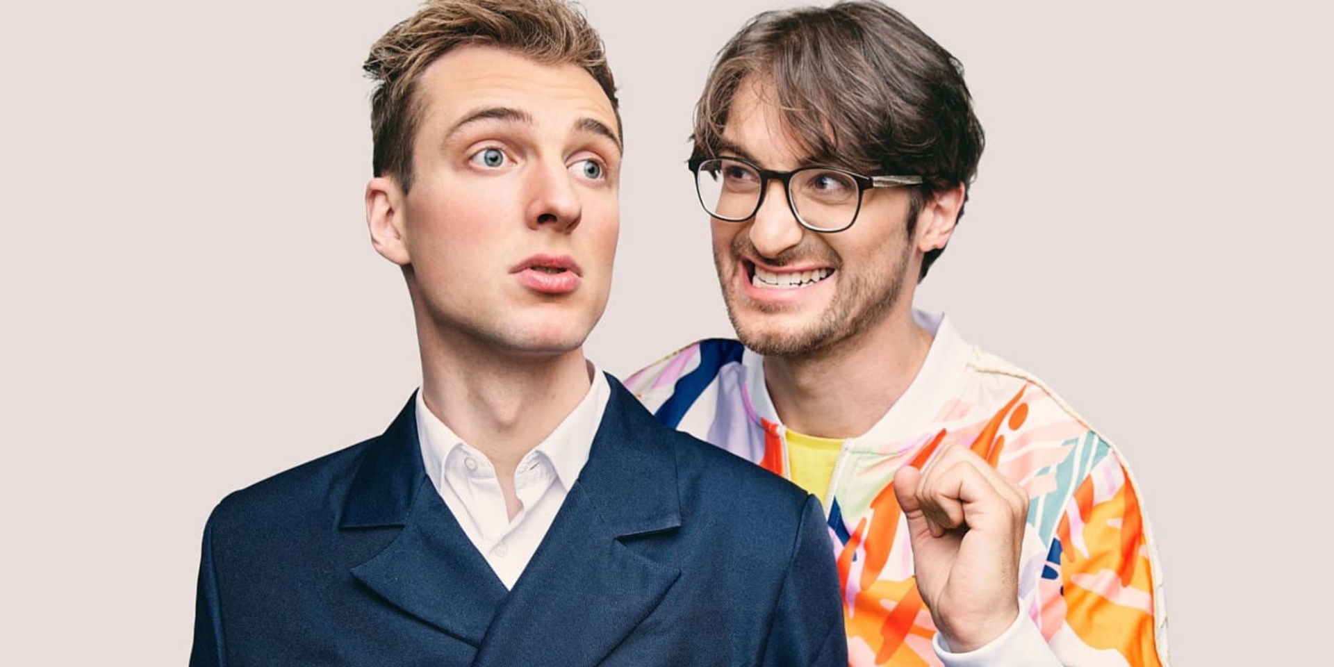 Zwei Männer nebeneinander. Einer trägt einen dunkelblauen Anzug, der andere einen bunten Anzug