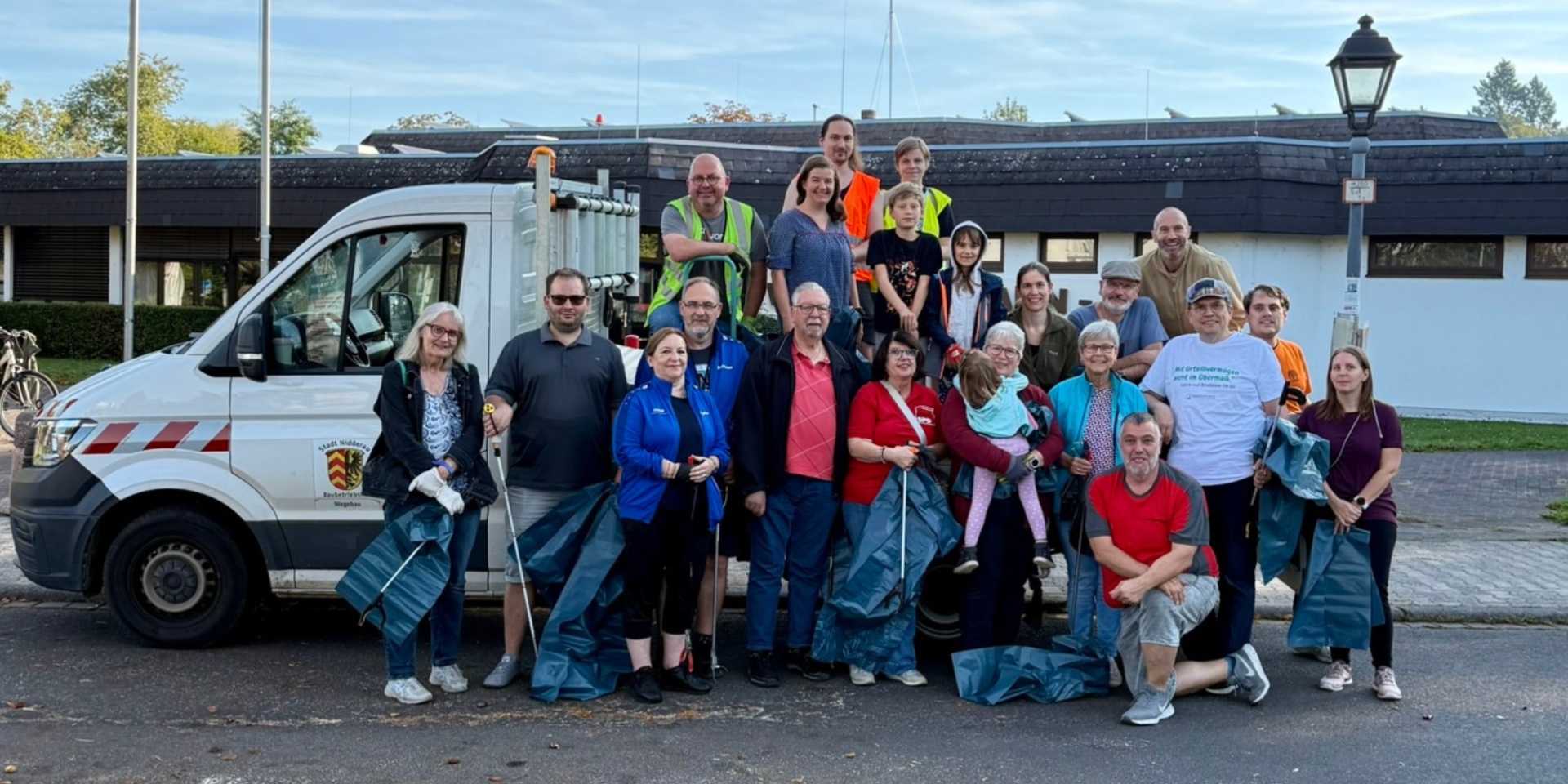 Personengruppe ausgestattet mit Mülltüten und Greifwerkzeug stehend vor einem Stadtfahrzeug.