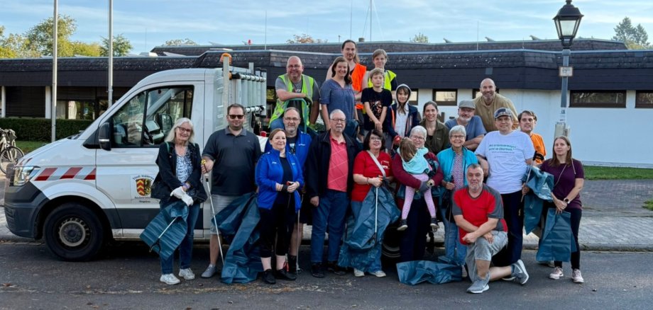 Personengruppe ausgestattet mit Mülltüten und Greifwerkzeug stehend vor einem Stadtfahrzeug.