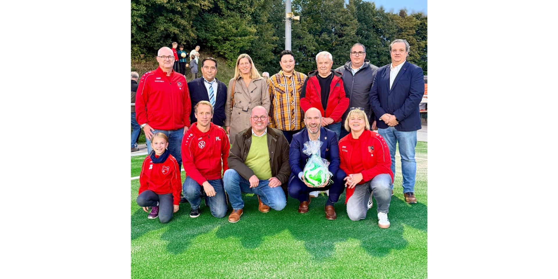 Eine Personengruppe zusammenstehend auf einem Kunstrasen. Ein Mann hält einen verpackten Fußball in der Hand.