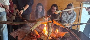 Mädchengruppe röstet Stockbrot über offenem Feuer.