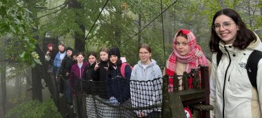 Mädchengruppe stehend auf einer Hängebrücke zwischen Baumwipfeln im Wald.