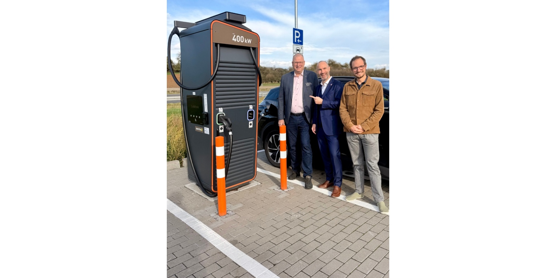 3 Männer stehend vor einer Schnellladesäule an einer Tankstelle
