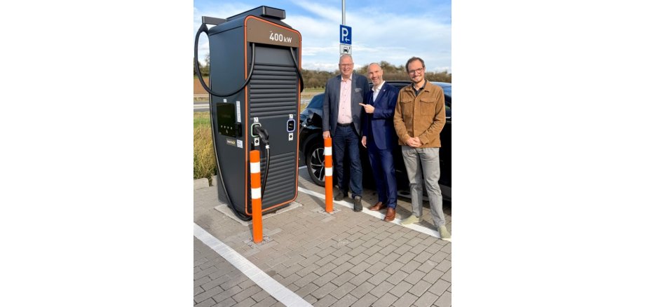 3 Männer stehend vor einer Schnellladesäule an einer Tankstelle