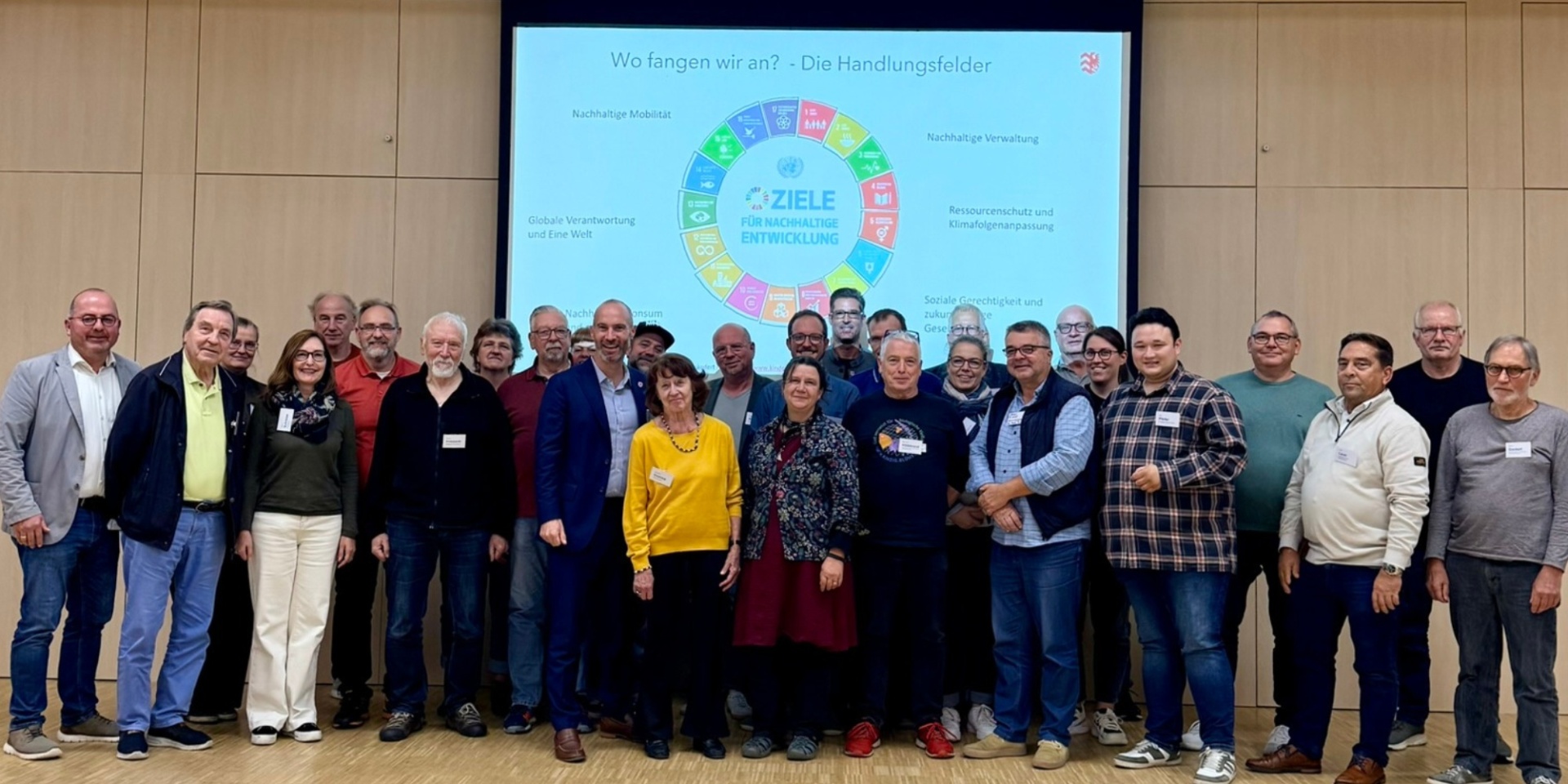 Mehrere Personen in einer Halle vor einer Leinwand stehend