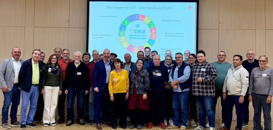 Mehrere Personen in einer Halle vor einer Leinwand stehend