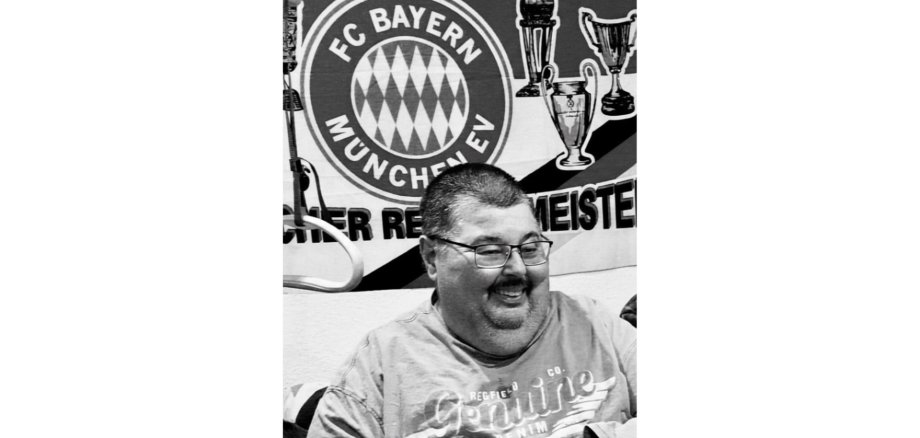 Schwarz-weiß Foto von einem Mann sitzend vor einem Fußball-Vereinslogo