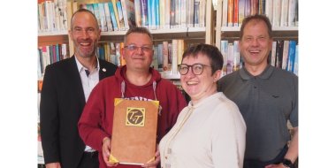 Eine Frau und drei Männer stehend vor einer Bücherwand.