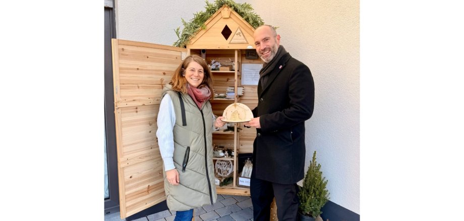 Ein Mann und eine Frau stehend vor einem kleinen Verkaufs-Häuschen aus Holz.