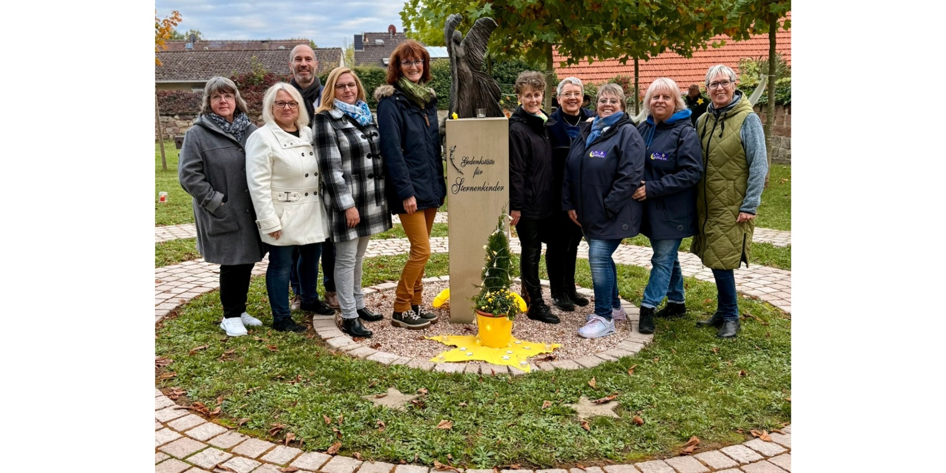 Ein Mann und neun Frauen stehend. In der Mitte ein Mahnmal aus Stein.