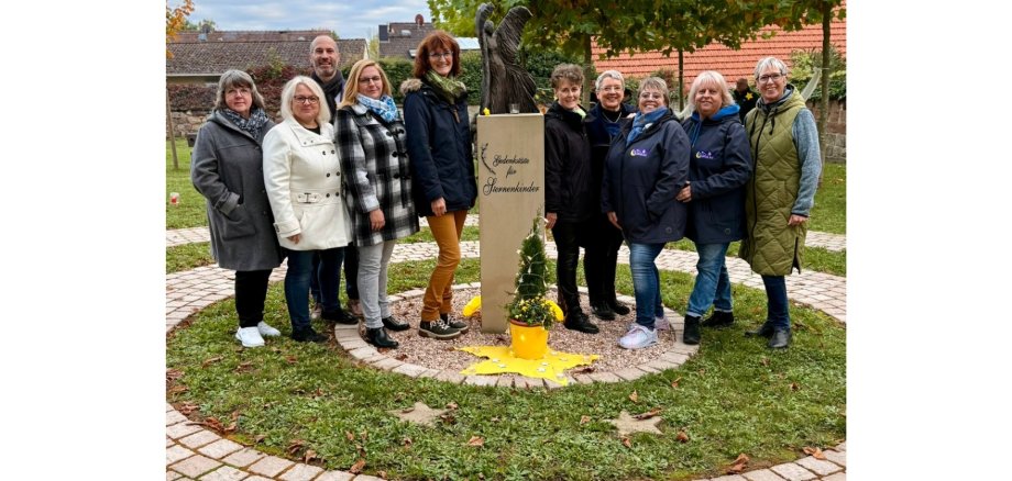 Ein Mann und neun Frauen stehend. In der Mitte ein Mahnmal aus Stein.