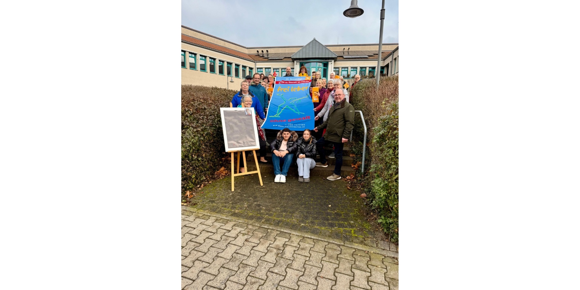 Mehrere Personen stehend vor einem Gebäude, eine Fahne haltend